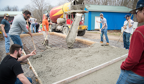 A class pours a concrete pad outside the Physical Plant.