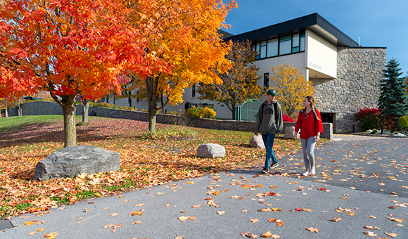 Two students walk outside of Wicks Hall on an autumn day.