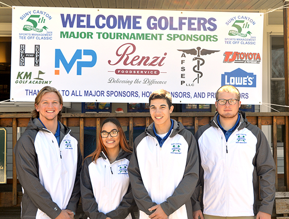 Four students stand in front of the Tee Off Classic Tourney sign.