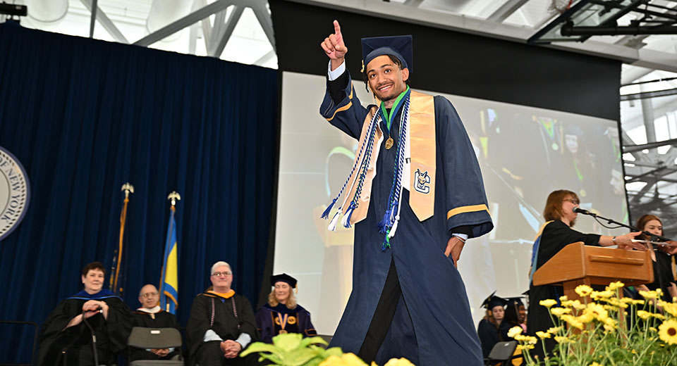 An excited graduate points out to the crowd while walking across the Commencement stage.