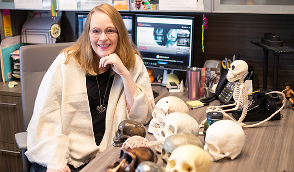 Kelly Ficner sits at her desk with many model skulls.