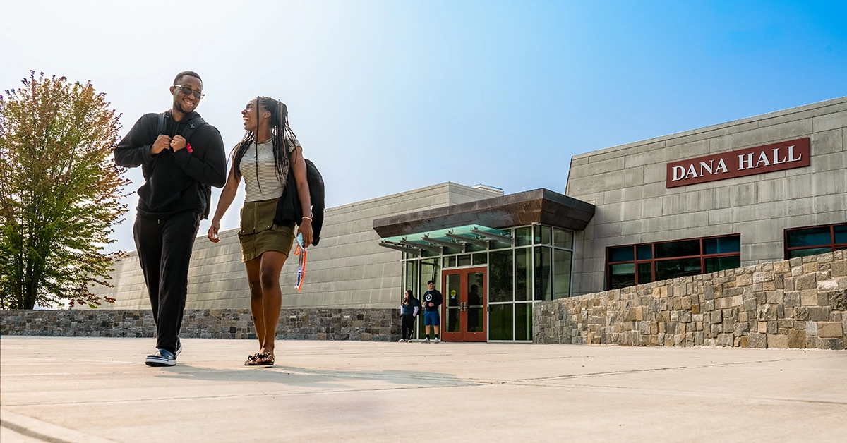 Two students laugh as they walk out of Dana Hall on a beautiful sunny day.