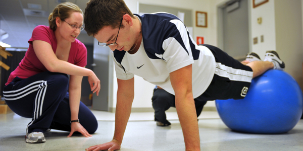 A PTA student assists a patient with push-up exercises.