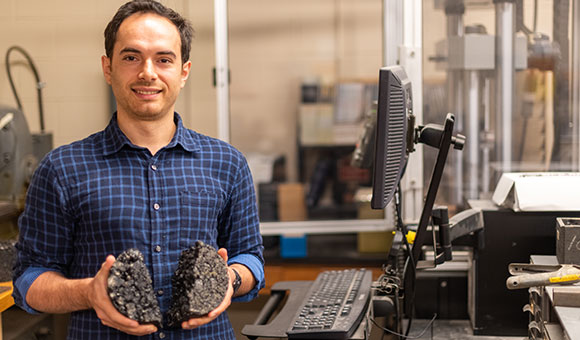 Aksel Seitllari holds a broken asphalt sample in the Material Strength testing lab.