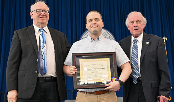 Chad Delosh accepts the Excellence in College Service Award from President Szafran and Chairman Ronald O'Neil.