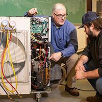 Dean Michael Newtown shows a student the internal components of a heat pump.