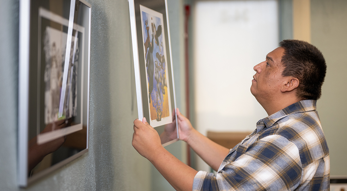 Honni David hangs his artwork in the Learning Commons classroom within Southworth Library.