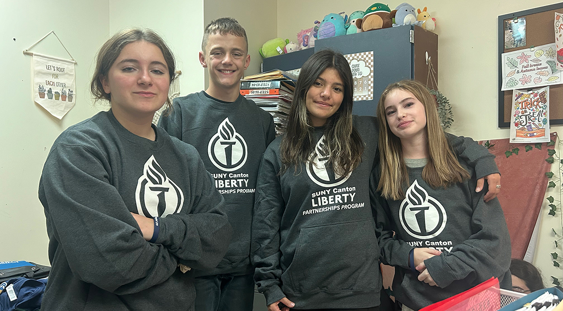 Four Liberty students pose for a photo with matching gray Liberty Partnerships sweatshirts.
