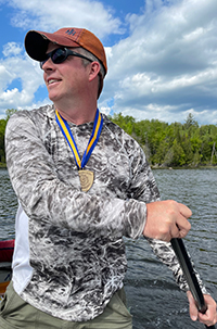 Matthew Burnett rows a canoe while wearing his Chancellor's Award medallion.