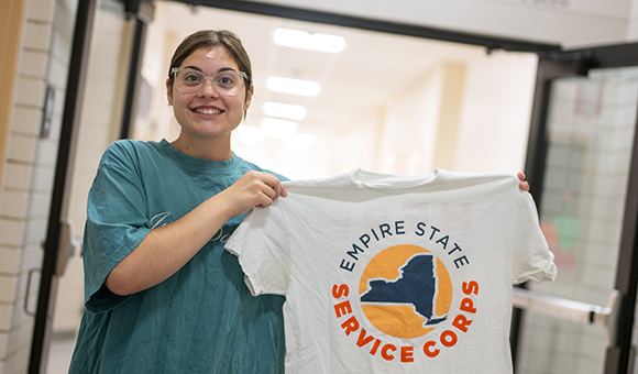 Olivia Rotundo holds up a white Empire State Service Corps t-shirt.