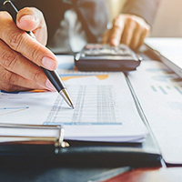 A person holding a pen uses a calculator to add a spreadsheet.
