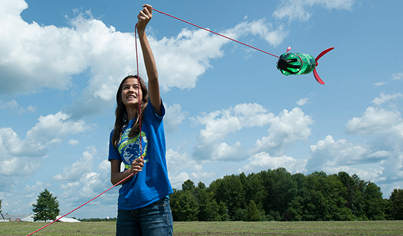 A student swings a bottle rocket on a string on a sunny day.