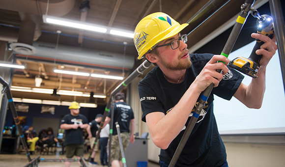 A student drills a bolt onto a steel bridge.