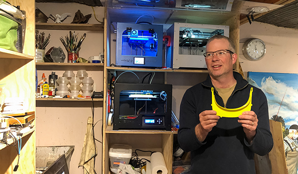 SUNY Canton Professor Matthew J. Burnett holds a piece of a face shield he printed in his Saranac Lake studio. Burnett has printed about 50 components for medical staff at regional hospitals.