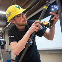 A student with a yellow hard hat builds a bridge.