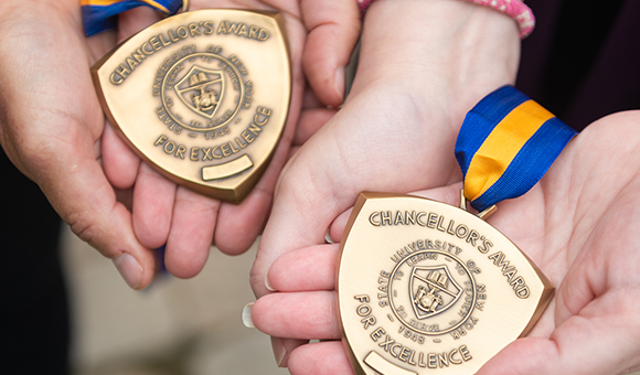 Renee Campbell and Kellie Harris hold their Chancellor's Award medallions in the palms of their hands.