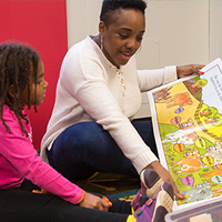 A teacher reads a large colorful book to a toddler.