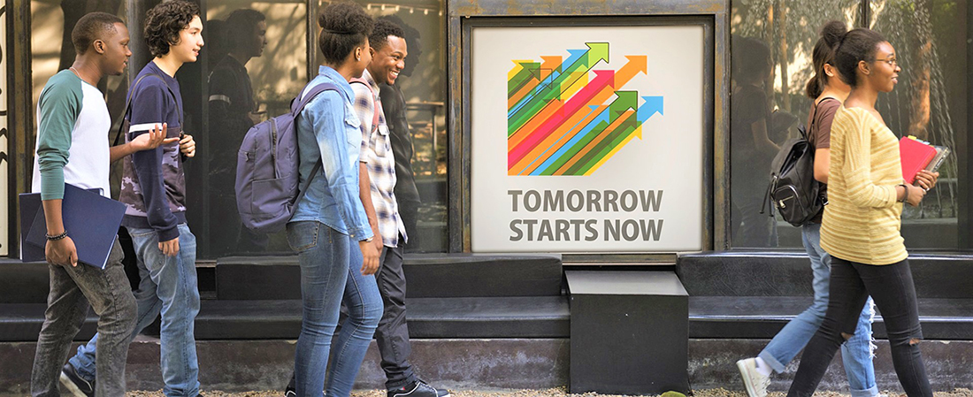 Students walking by a sign that says Tomorrow Starts Now.