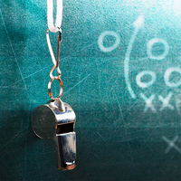 A whistle hangs in front of X's and O's on a chalkboard.