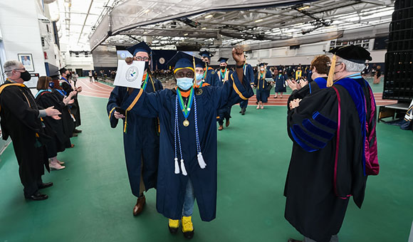 A student holds his diploma up in victory while faculty look on.