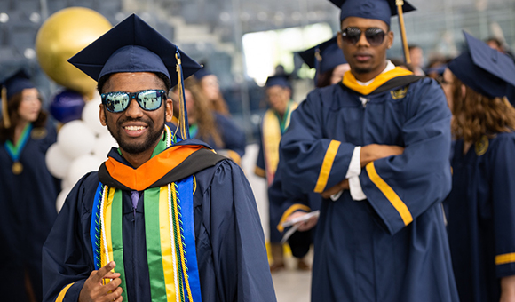Two graduates wearing sunglasses smile and pose before the Commencement Ceremony.