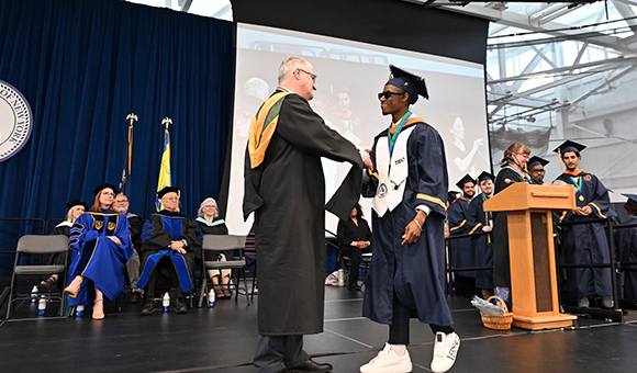 Dean Michael Newtown shakes a graduate's hand on stage during Commencement 2025.