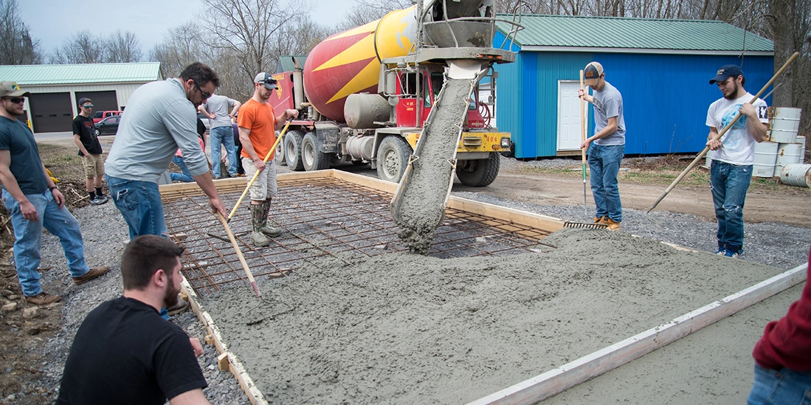 A class pours a concrete pad outside the Physical Plant.