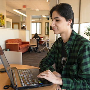 A Cybersecurity students studies on his laptop near a window in Southworth Library.