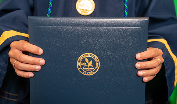 A person holds a diploma with a golden SUNY Canton seal is embossed on the cover.