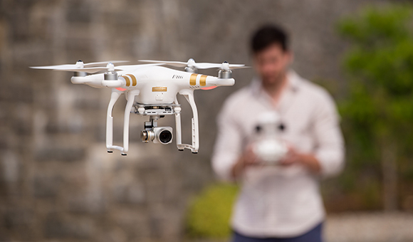 A drone hovers while the pilot is seen in the background.