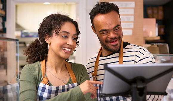 A woman trains a man with down syndrome how to use a checkout system.