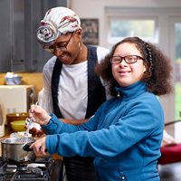 A woman assists a girl with special needs in a kitchen.
