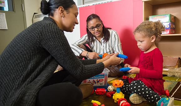 Two students work with a toddler on development activities.