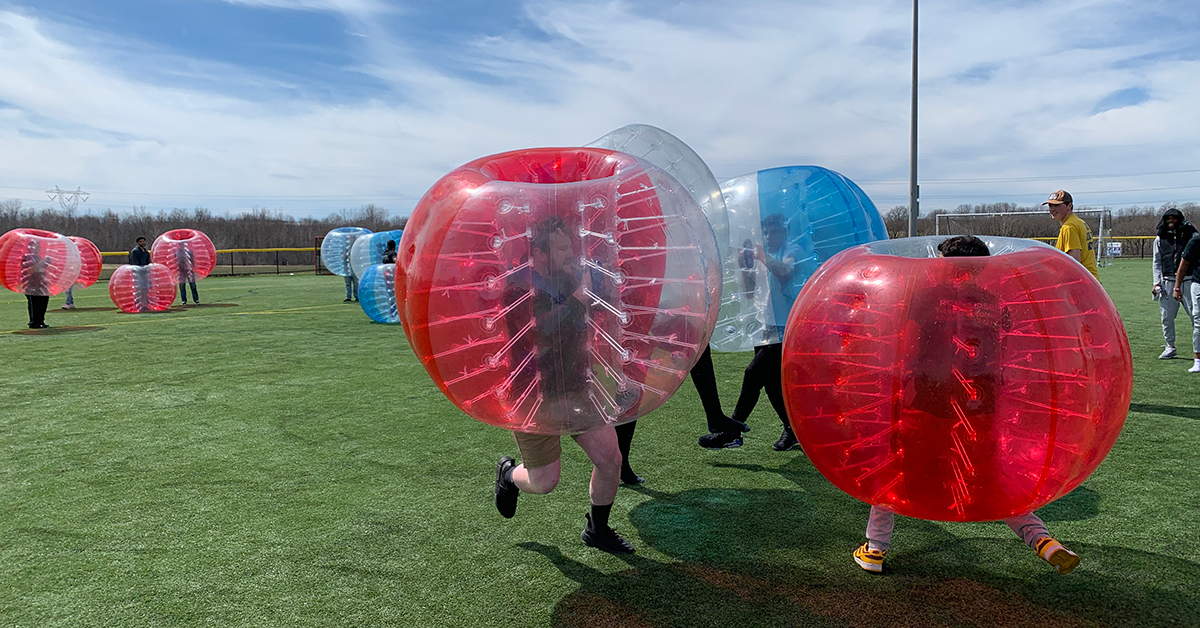 Students competing in bubble soccer collide on the turf field.