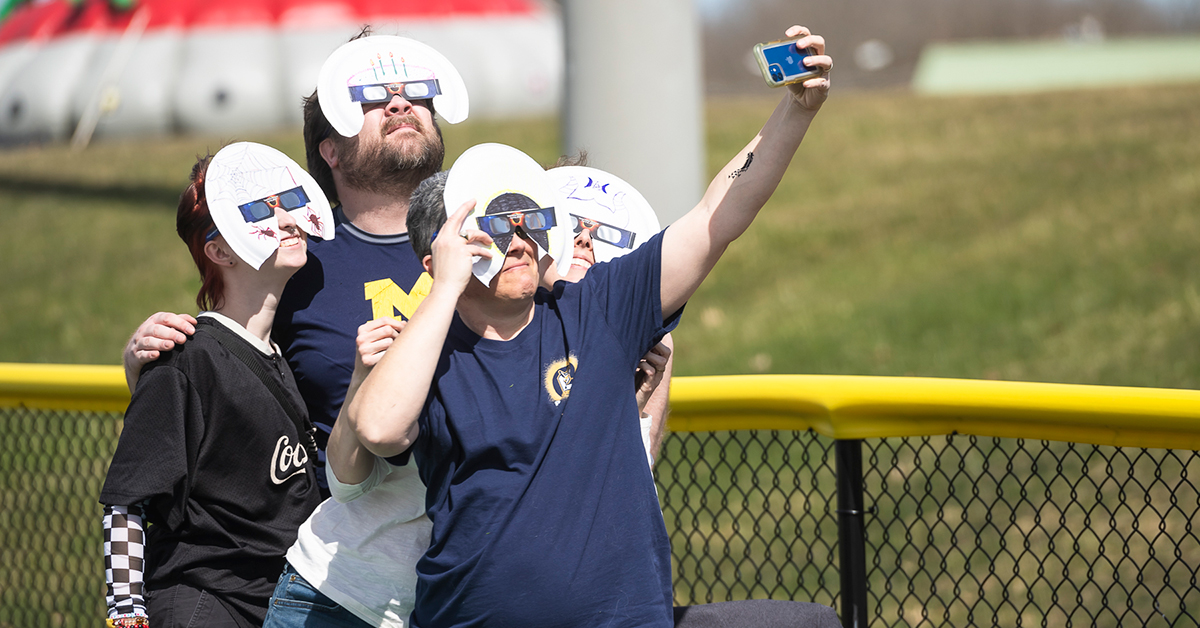 Students with paper plate cutouts and eclipse glasses gaze upon the sun.