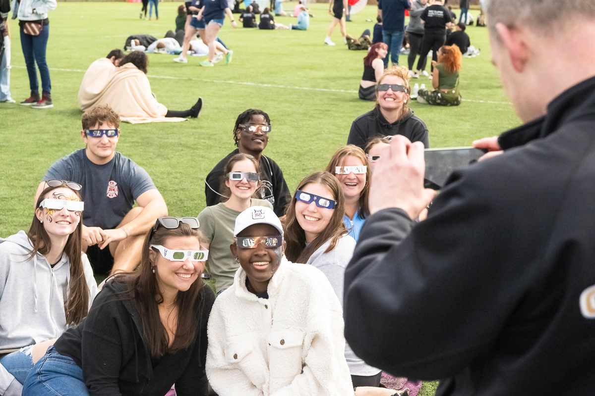 Several students pose with their eclipse glasses on the turf field.