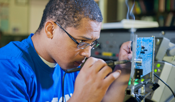 A student solders a motherboard.