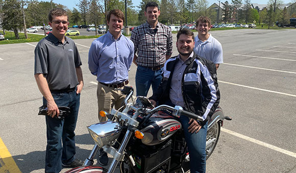 A group of students stand around their Mechanical Capstone project, an electric motorcycle.