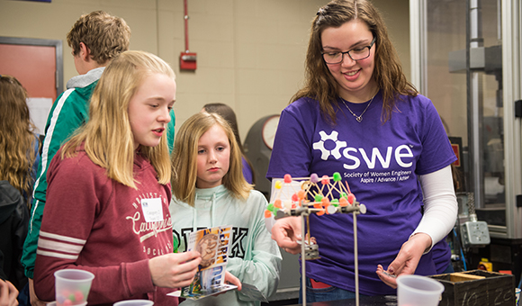 A SUNY Canton students assists two younger students in building a tower made from gum drops and spaghetti.