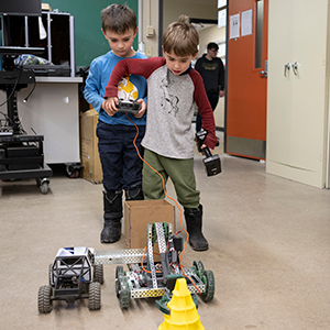 wo students attempt to grab a yellow cone with a mobile robotic arm.