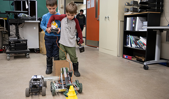 Two students attempt to grab a yellow cone with a mobile robotic arm.