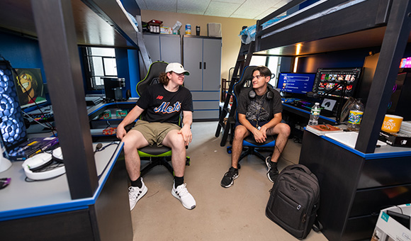 Two students sit in gamer chairs in their new Esports Wing room.