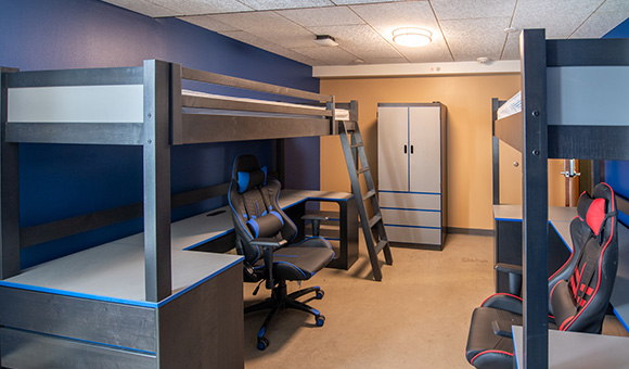 Esports Wing room with blue and gold walls, elevated beds, and gaming chairs.