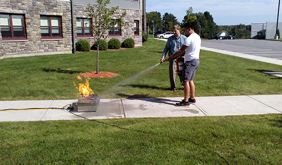 A student practices with an extinguisher on a sidewalk.