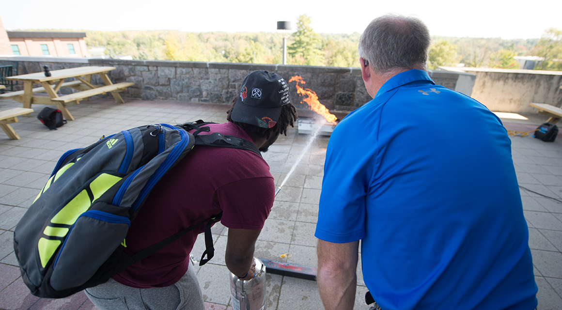 A student is trained on proper fire extinguisher use in the campus plaza.