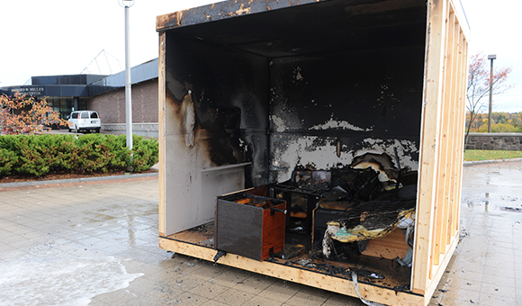 A fully extinguished mock burn dorm room with charred walls.