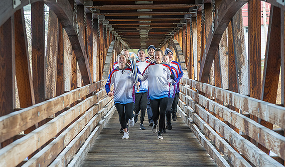 SUNY Canton athletes run the FISU torch across the footbridge.