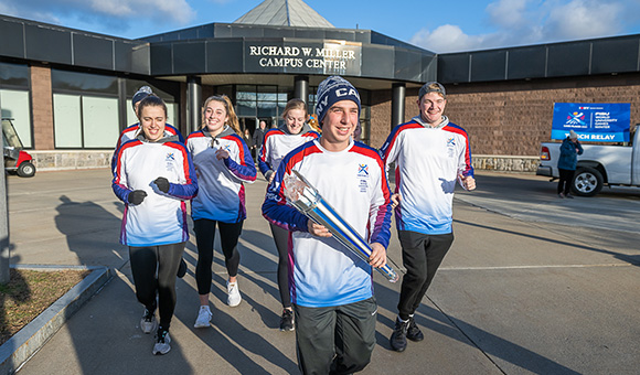 SUNY Canton athletes led by Tyler Fuentes runs with the FISU torch outside the Miller Campus Center.