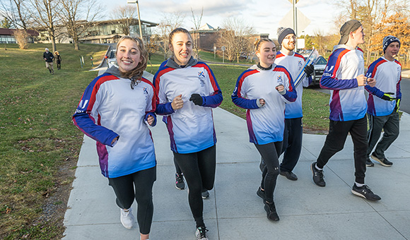 SUNY Canton athletes run the FISU torch down the ramp near Nevaldine Hall.