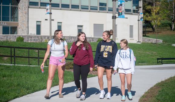 Four students walk together outside French Hall on a bright fall day.